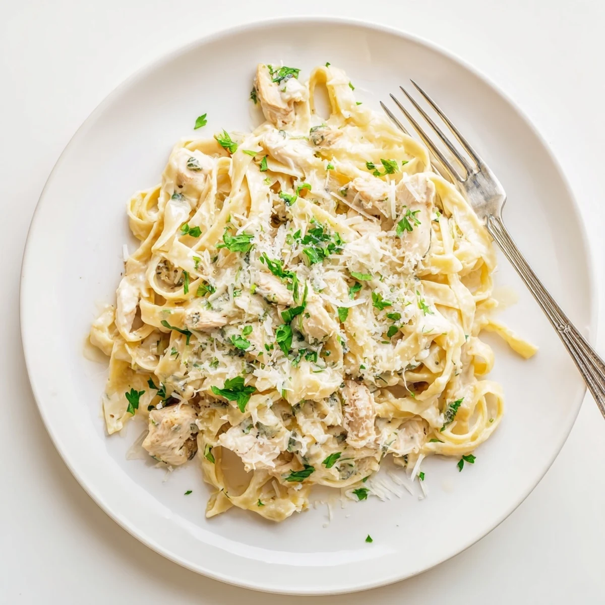 Slow cooker chicken Alfredo dish garnished with fresh parsley and served steaming hot in a white ceramic bowl