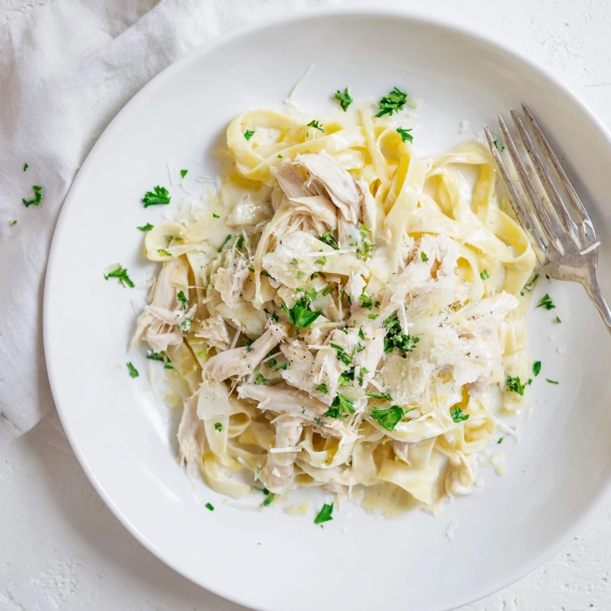 Close-up of Crock Pot Chicken Alfredo showing shredded chicken pieces coated in thick creamy sauce over twirled fettuccine noodles