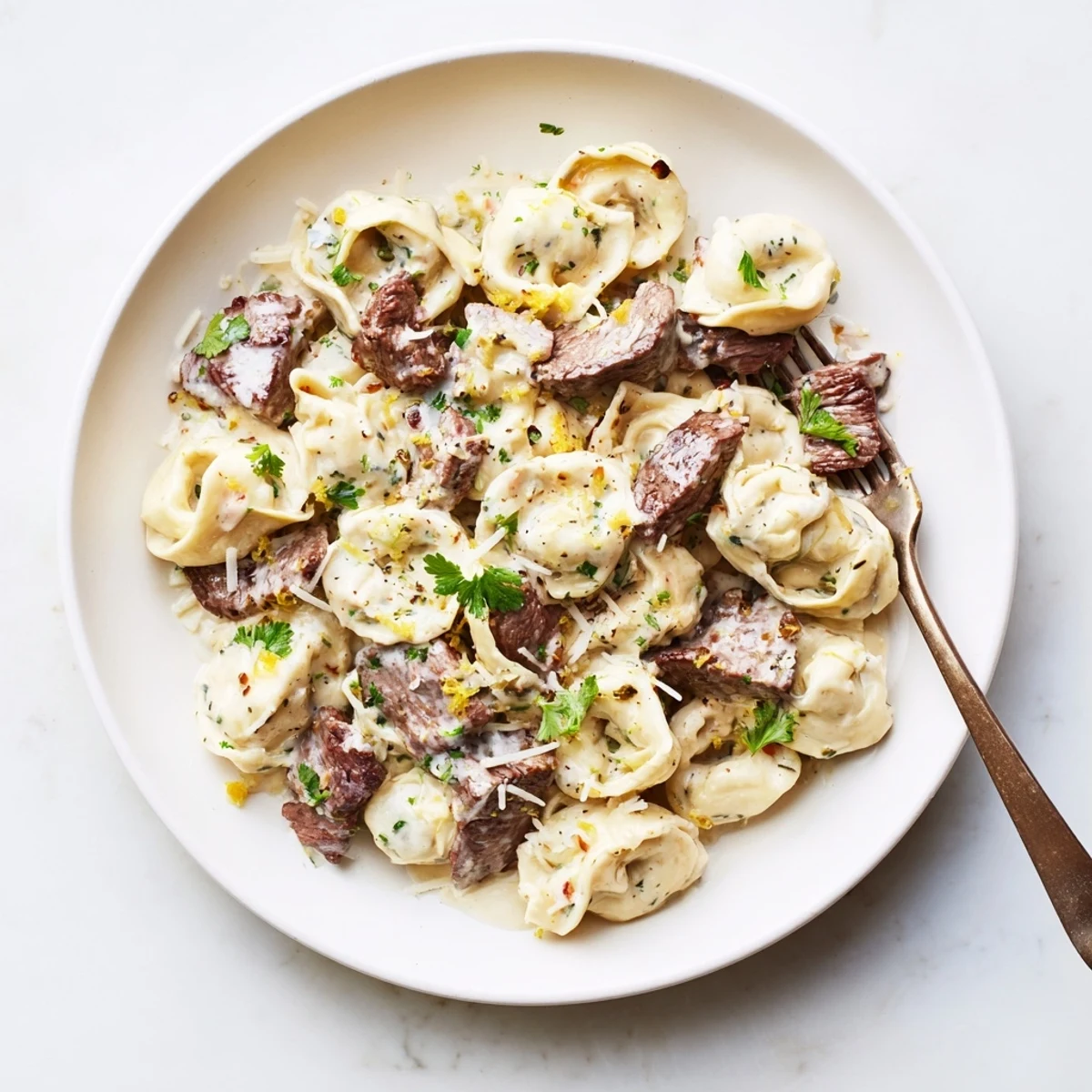 Golden seared steak slices atop cheese tortellini coated in velvety garlic creamhouse sauce with fresh parsley garnish