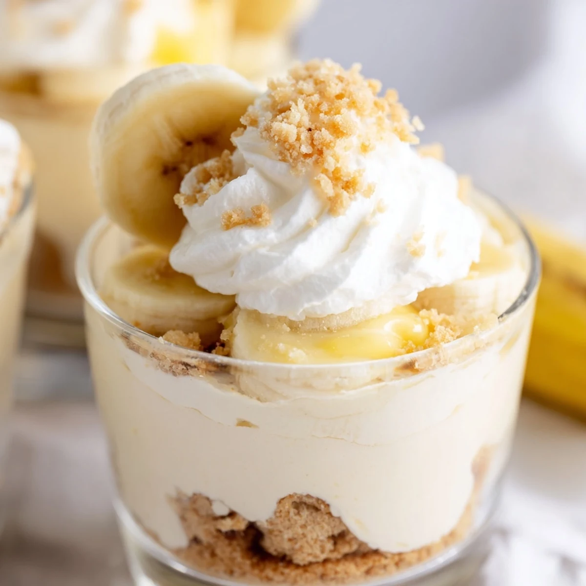 Creamy banana pudding cheesecake cups layered with vanilla wafer crumbs in clear glass jars