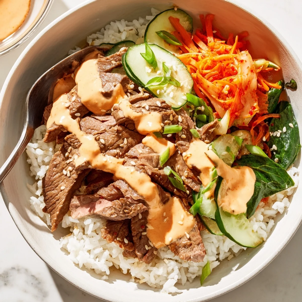 Caramelized steak slices over fluffy jasmine rice drizzled with spicy cream sauce in Korean BBQ steak rice bowls