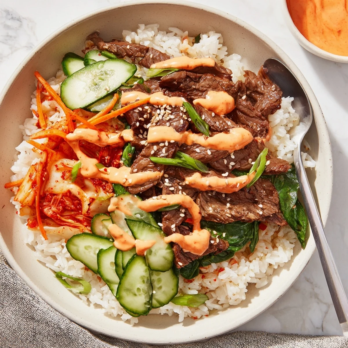 A generous Korean BBQ steak rice bowl topped with crisp julienned veggies, kimchi, and a creamy Sriracha drizzle