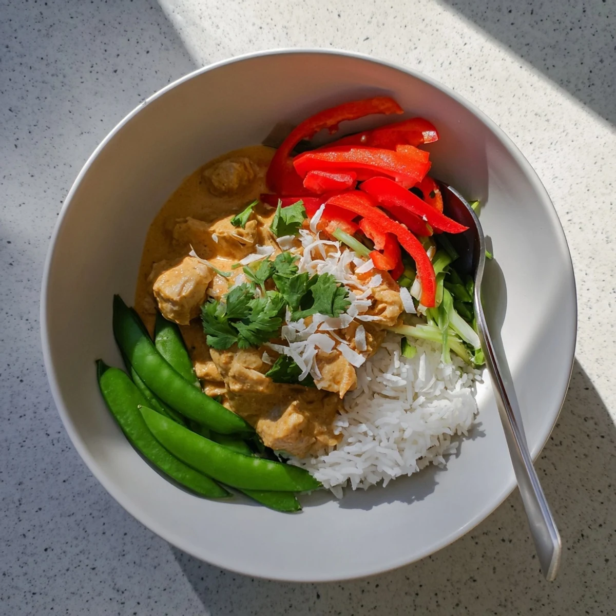 Golden coconut chicken rice bowl topped with fresh cilantro and crispy vegetables in a creamy white sauce