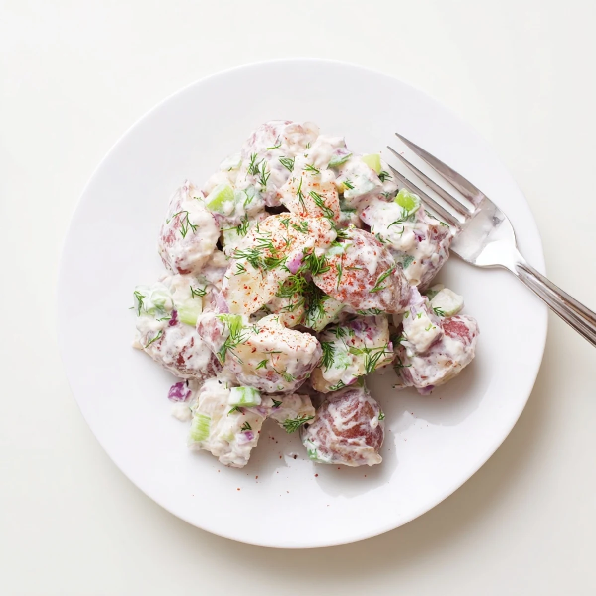 Colorful red potato salad featuring fresh red onions, parsley, and dill in a creamy mustard dressing.