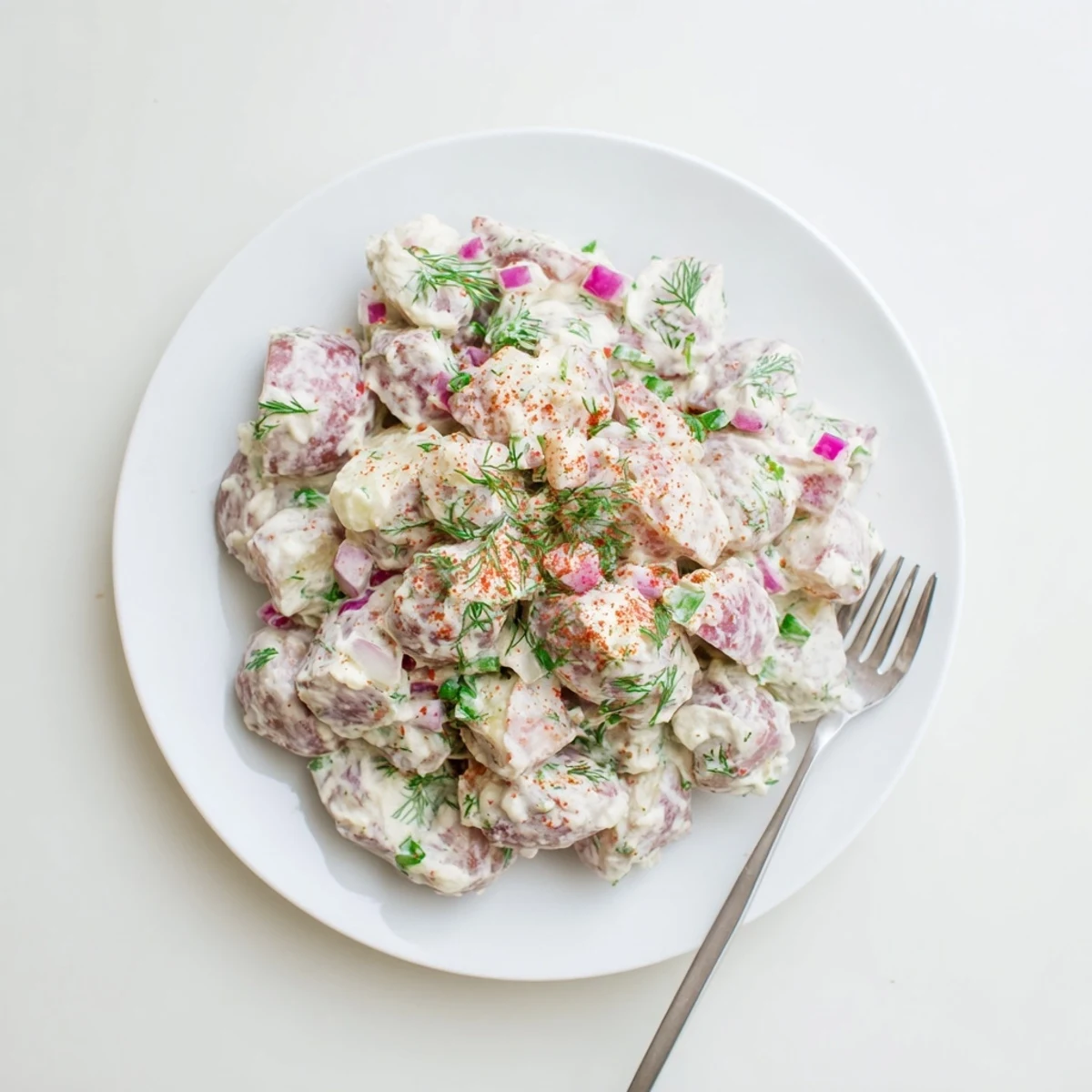 Hearty red potato salad displayed in a white bowl, garnished with herbs for summer picnics.