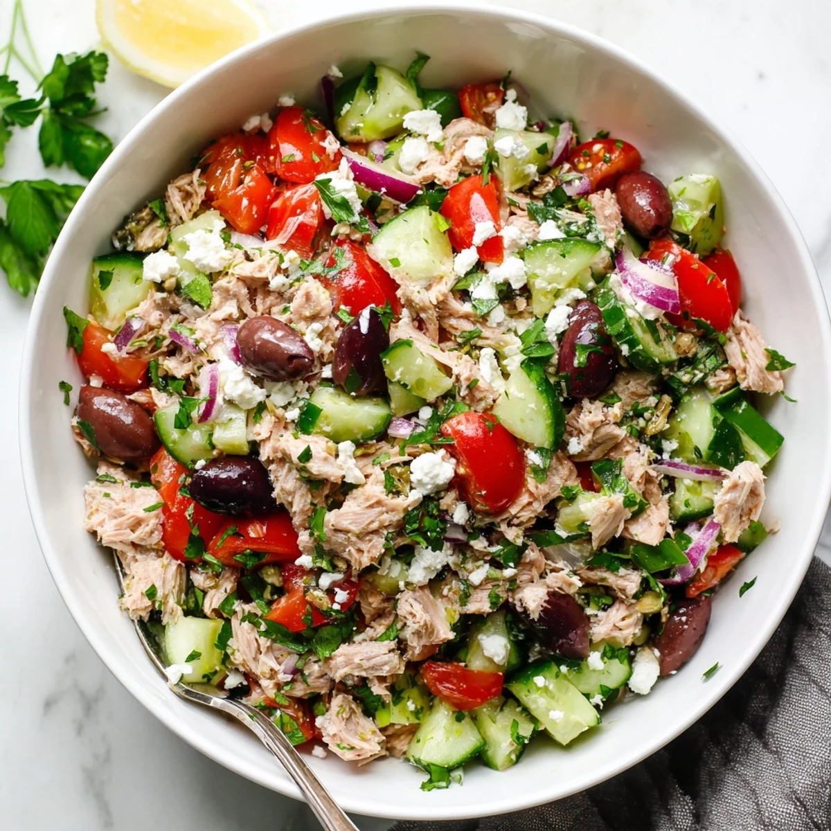 Fresh Mediterranean tuna salad bowl with chunky tuna, crisp vegetables, olives, and zesty lemon dressing garnished with green herbs.