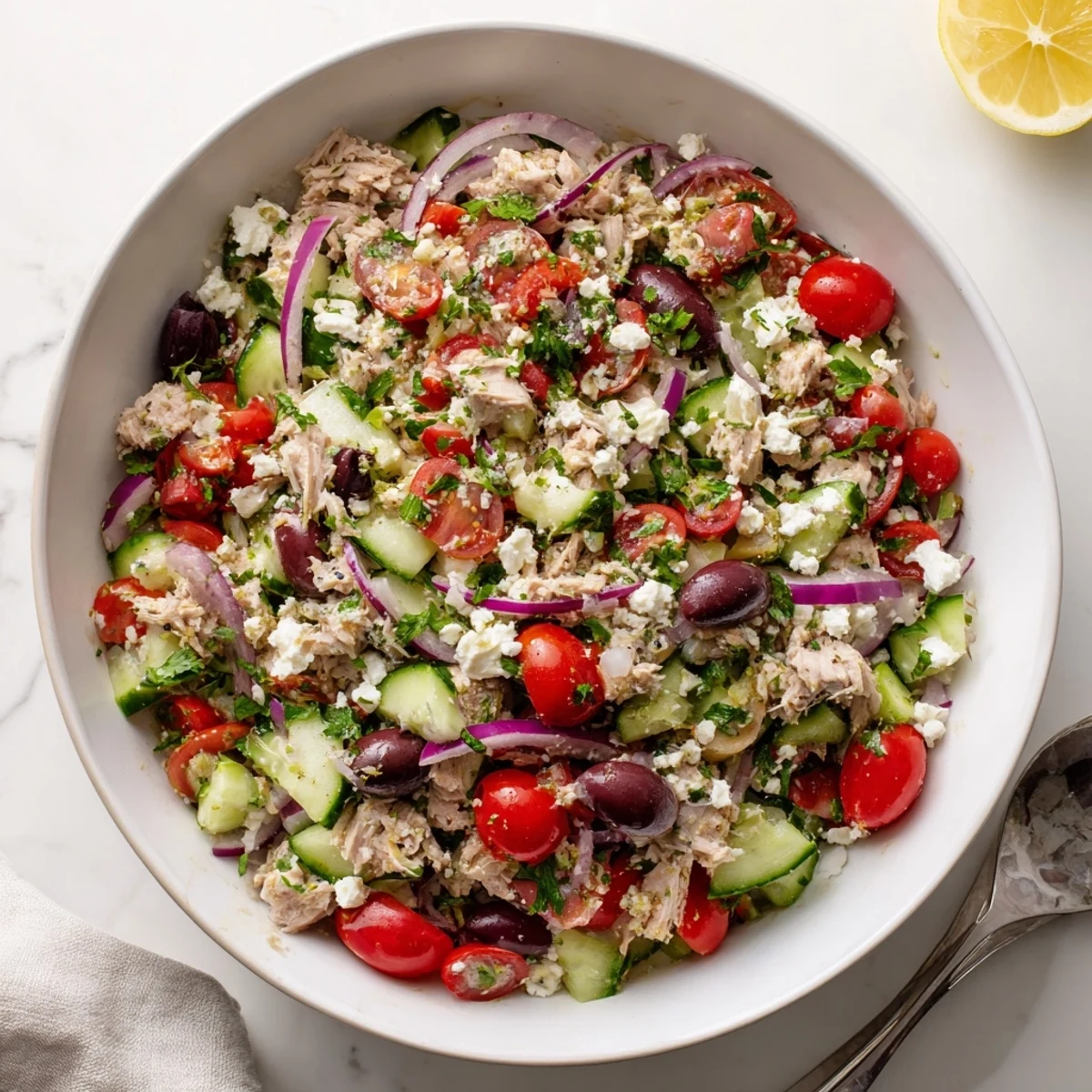 Colorful plate of protein-packed Mediterranean tuna salad featuring tender tuna, cherry tomatoes, cucumber, and crumbled feta cheese drizzled with olive oil.
