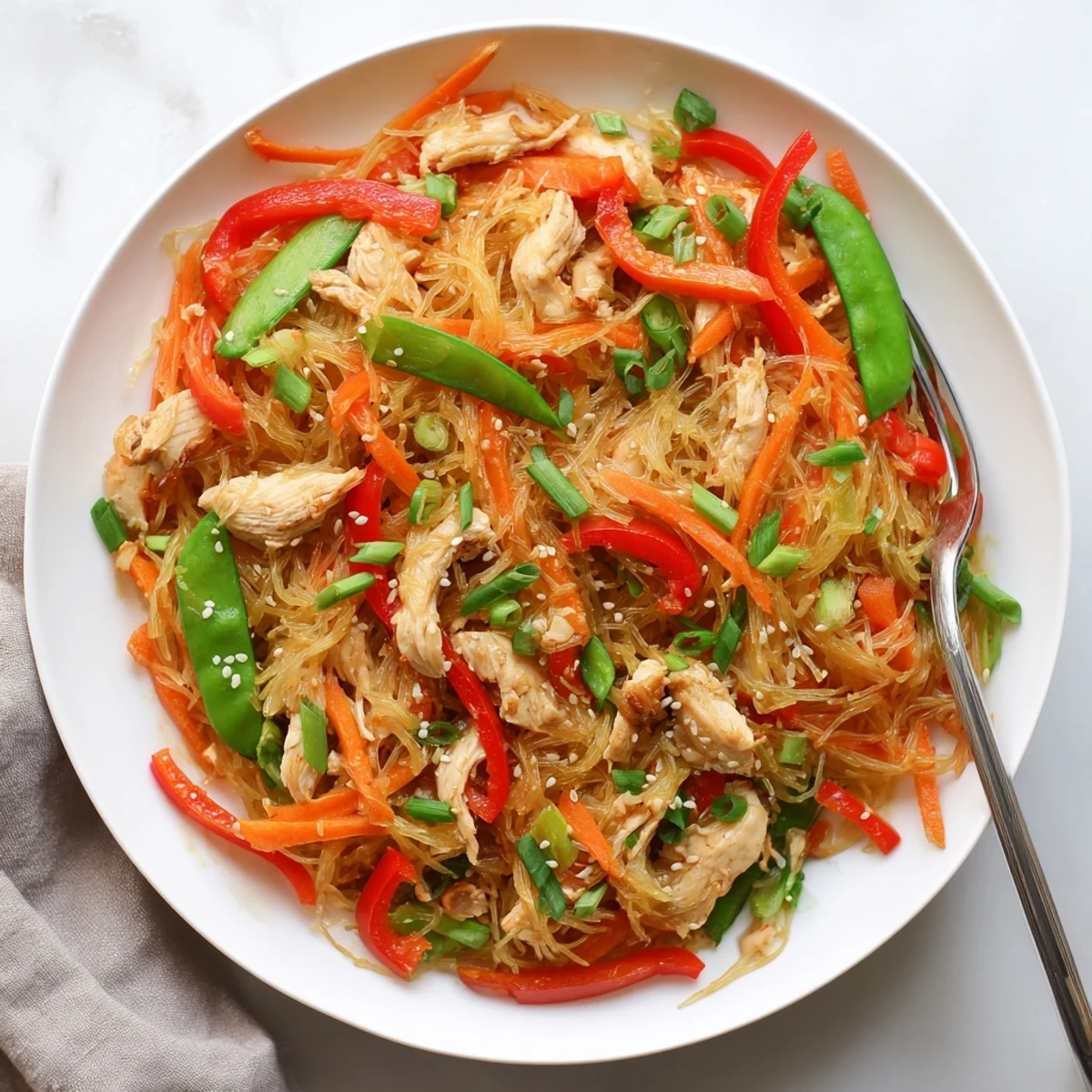 Gluten-free spaghetti squash chicken chow mein served in white bowl with snap peas carrots and sesame garnish