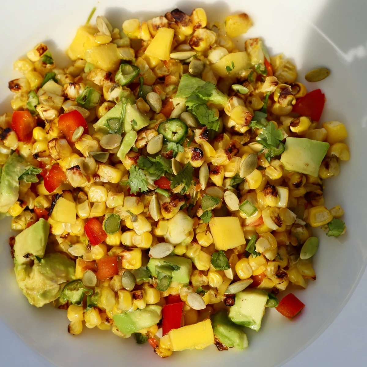 Refreshing tropical charred corn and avocado salad tossed with lime dressing and topped with toasted pumpkin seeds