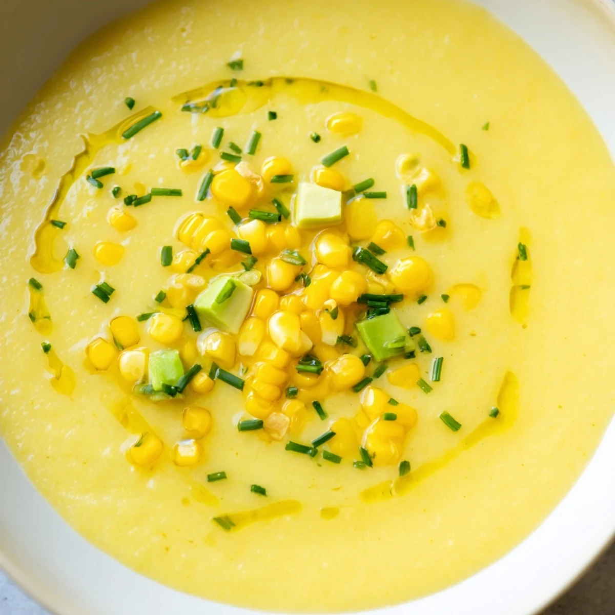 Golden summer sweet corn gazpacho served chilled in a rustic bowl with fresh herb garnish