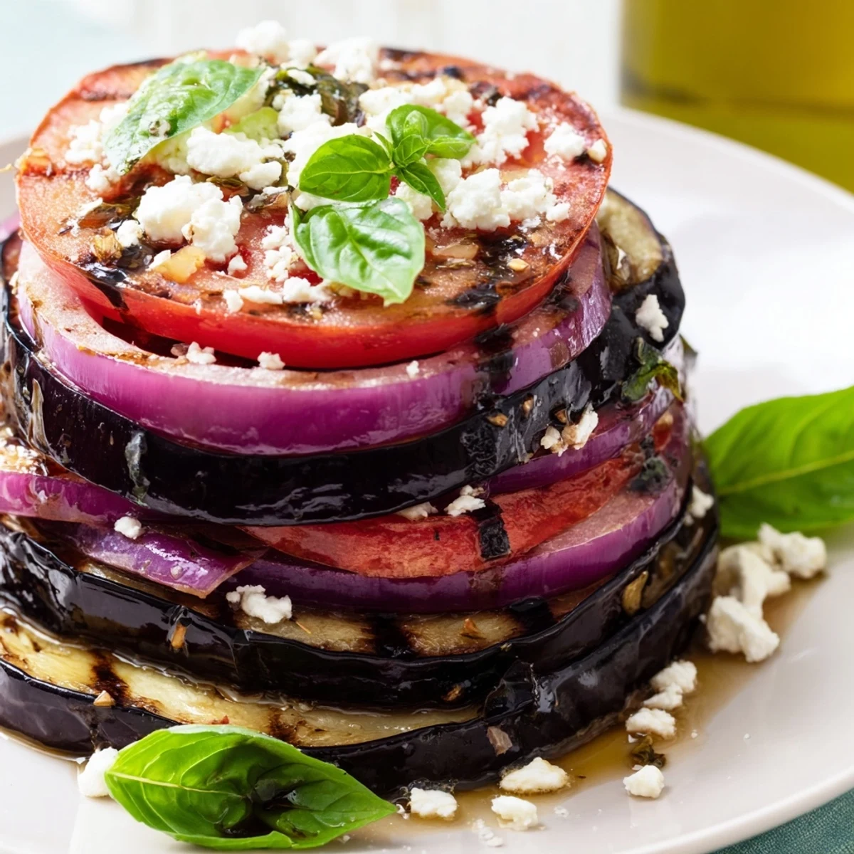 Smoky grilled tomato eggplant stacked on a platter with fresh basil and crumbled feta cheese